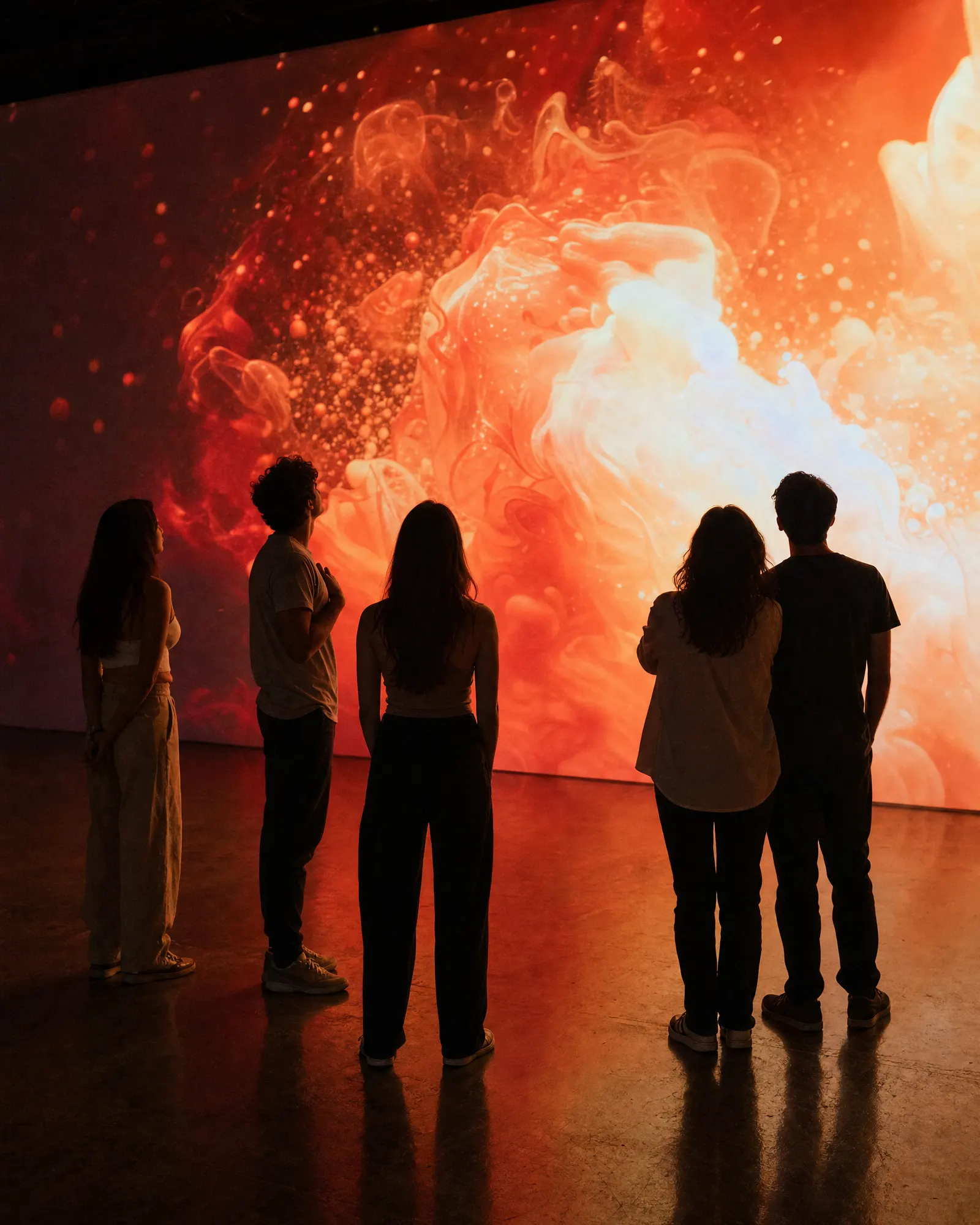 A small group looking up at a large warm abstract light projection in a dark gallery