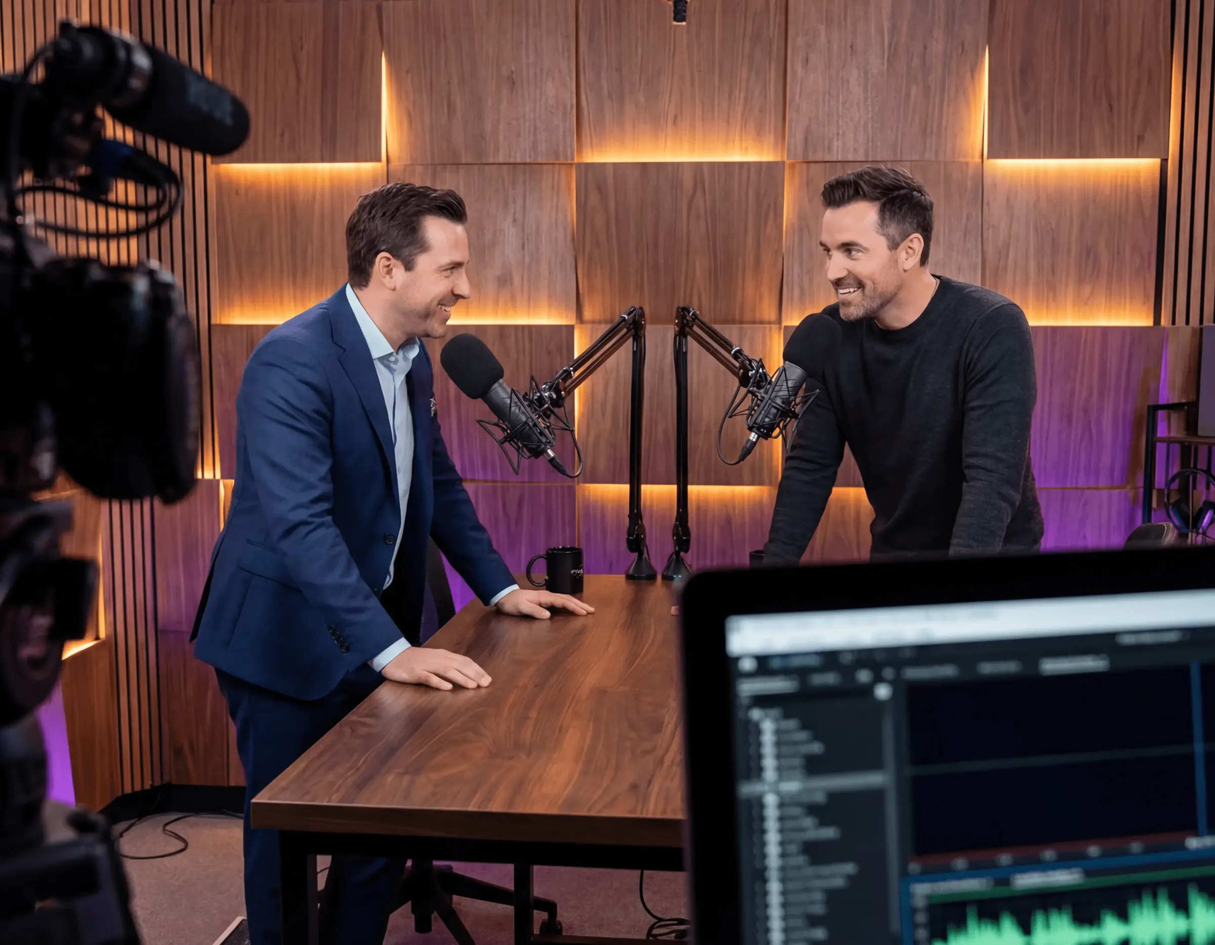 Two men recording a podcast interview across a wooden table with microphones
